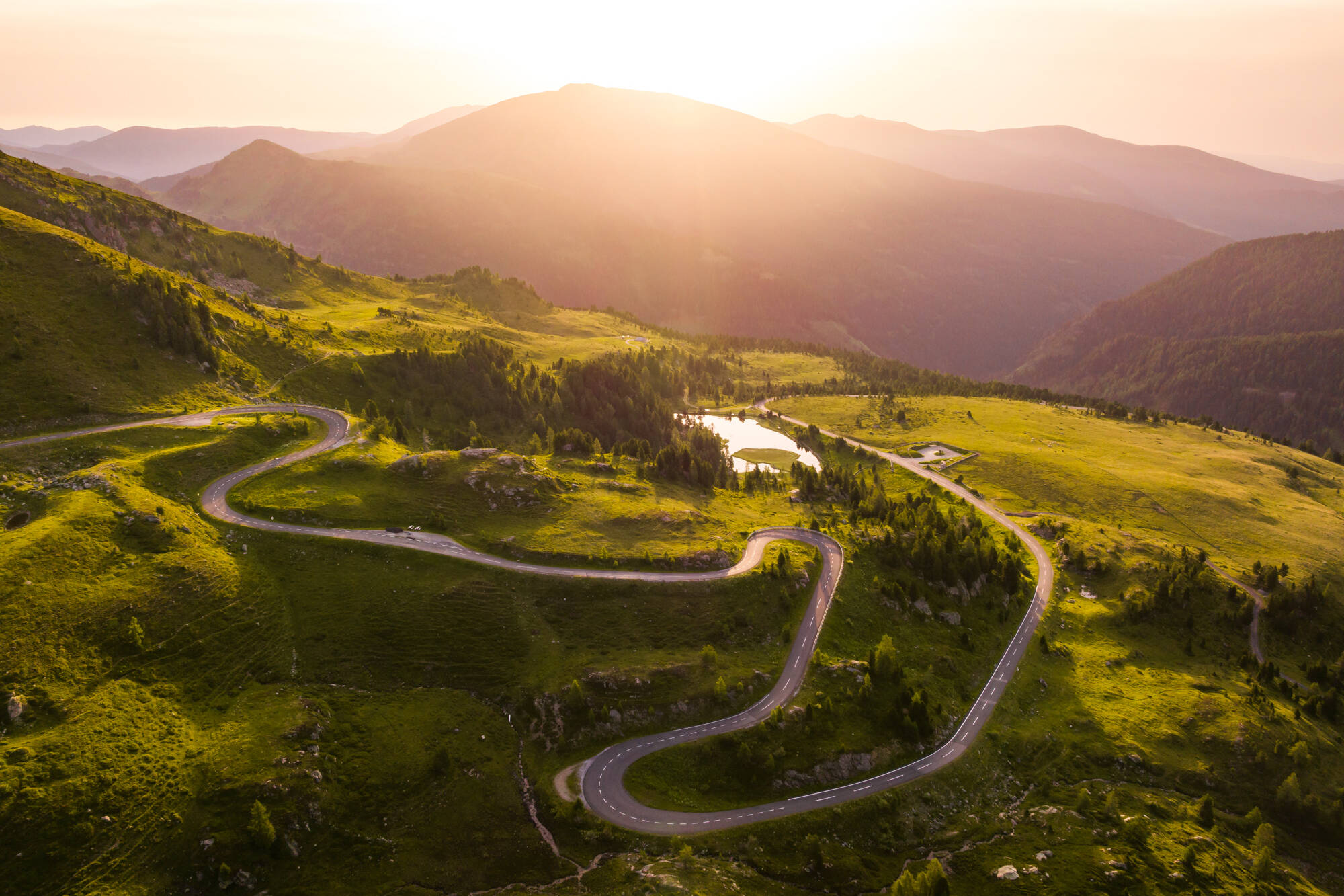 Kurvenreiche Bergstraße im goldenen Abendlicht, Luftaufnahme