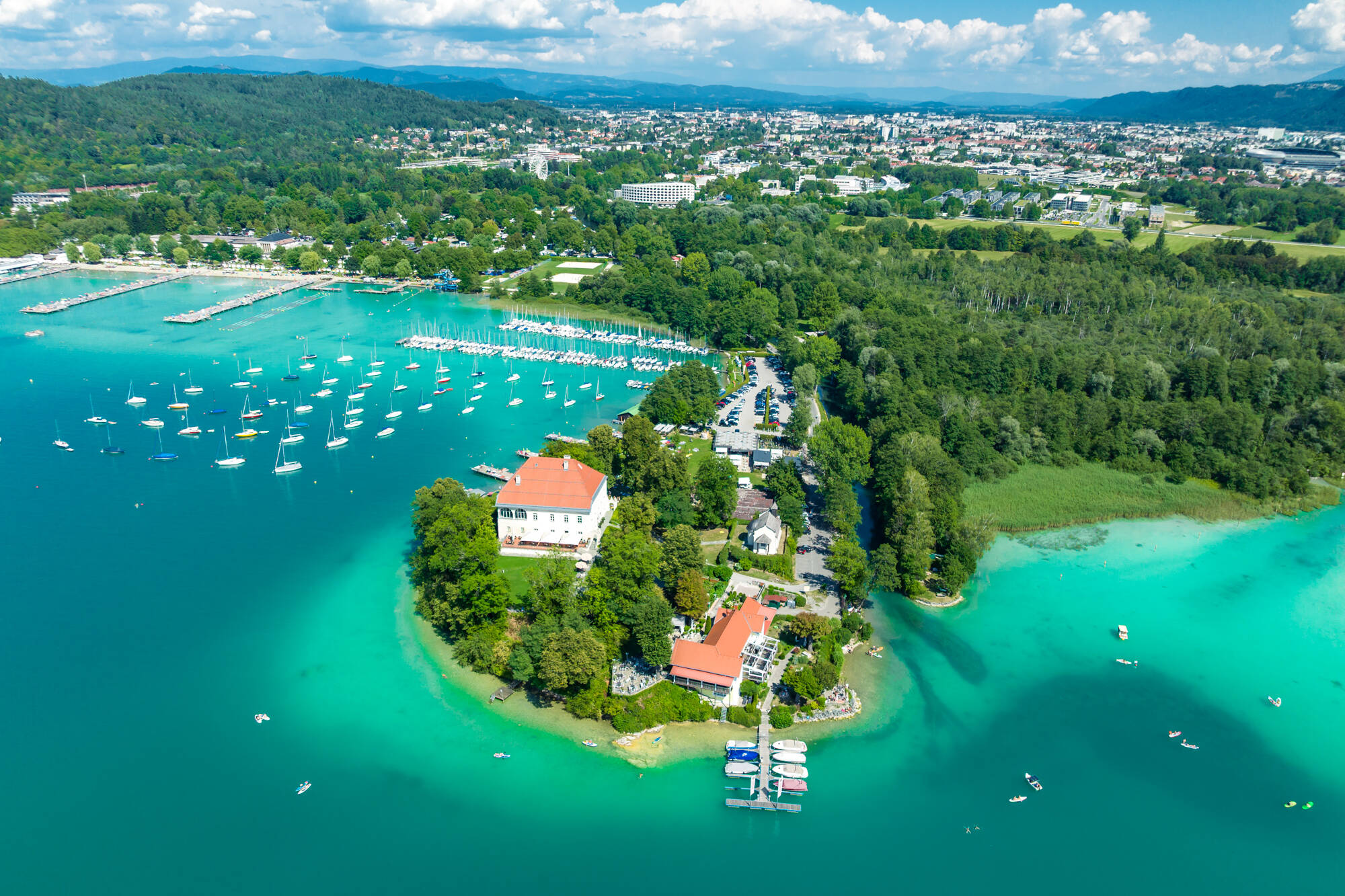Luftaufnahme einer Halbinsel mit Villa, Bootshafen und türkisblauem See
