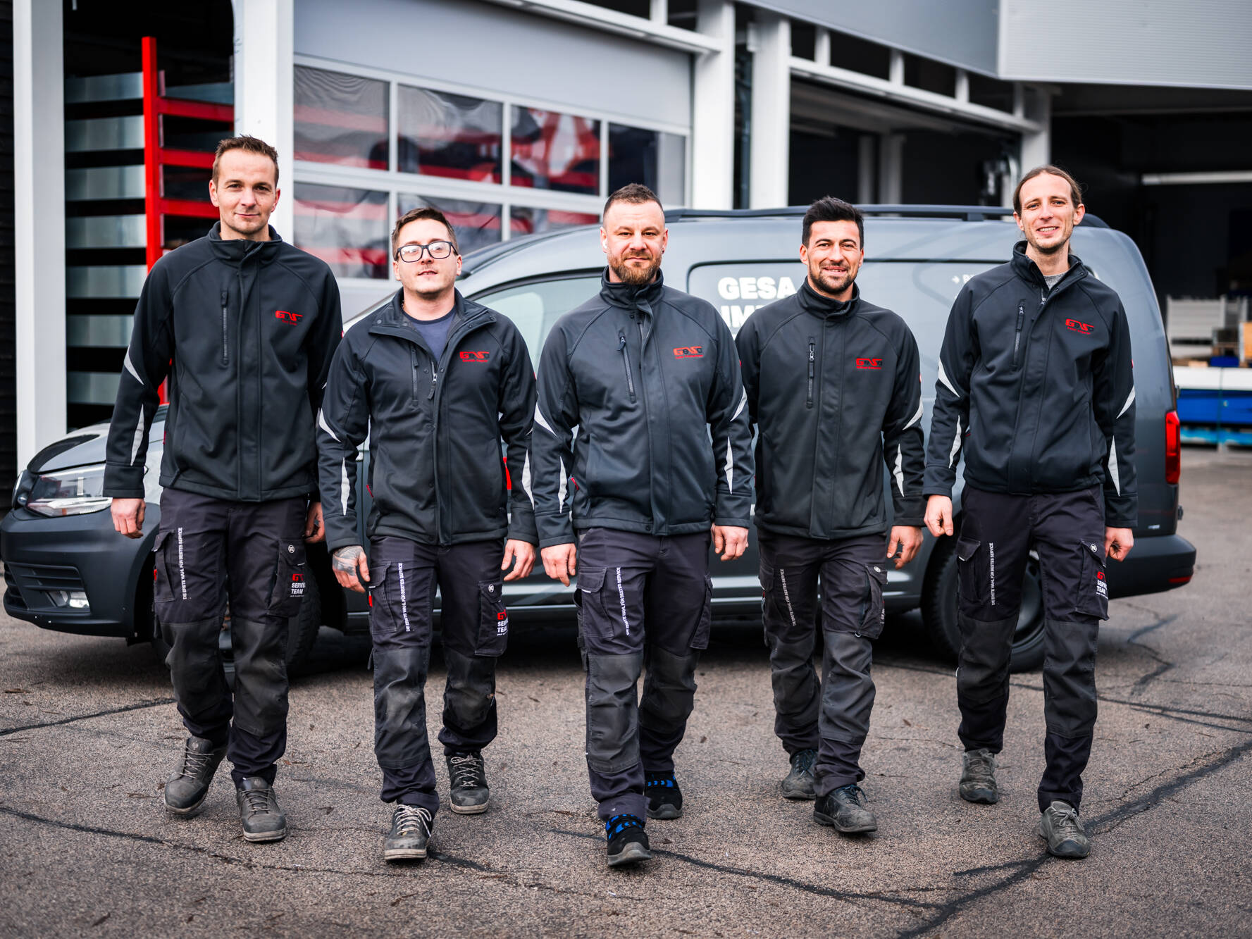 Fünf Mitarbeiter in Arbeitskleidung vor einem Firmenwagen – Teamfoto