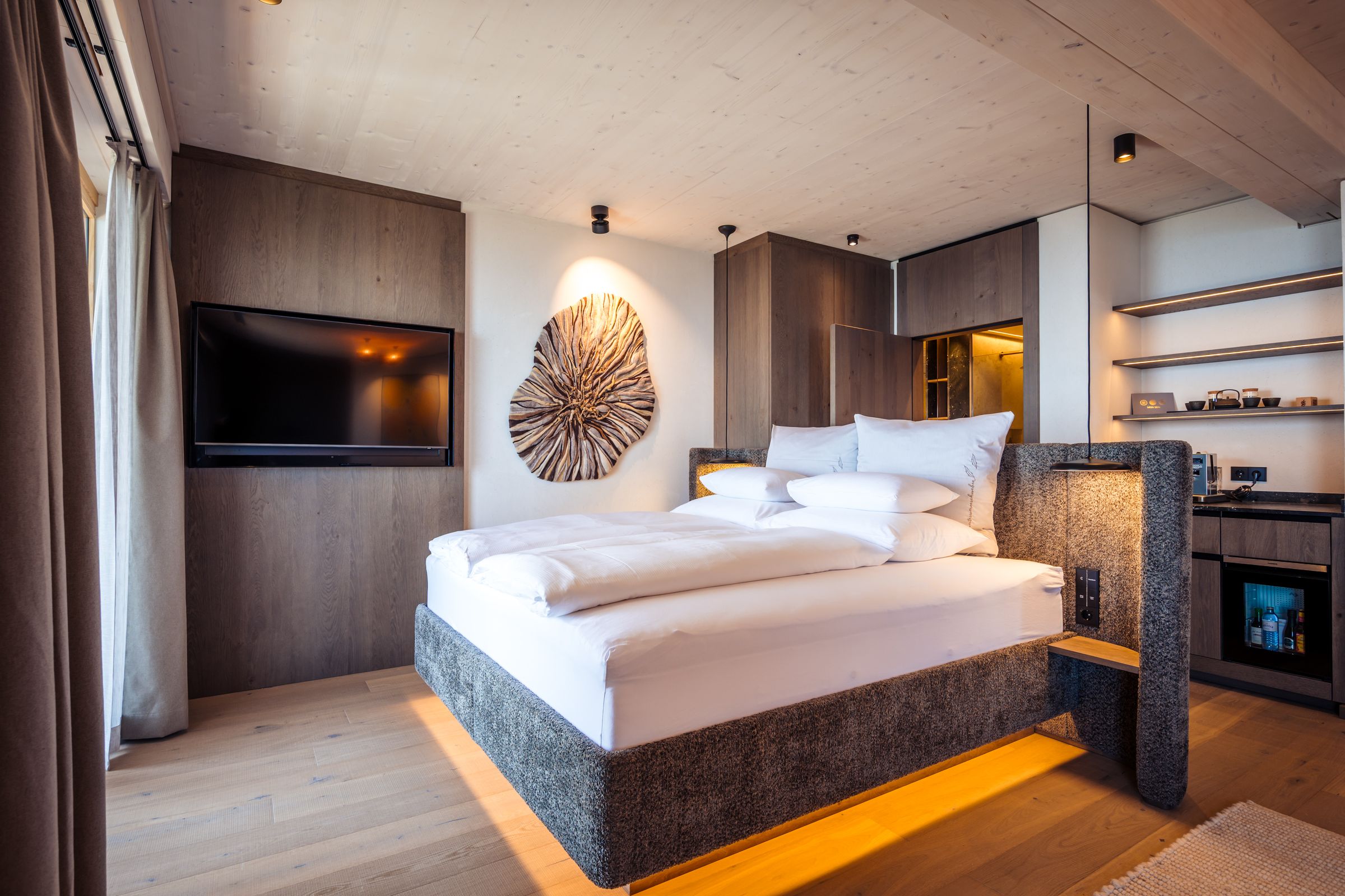 Hotelzimmer im Mountain Resort Feuerberg mit Holz, Doppelbett mit beleuchtetem Sockel und indirektem Licht – Architekturfotografie