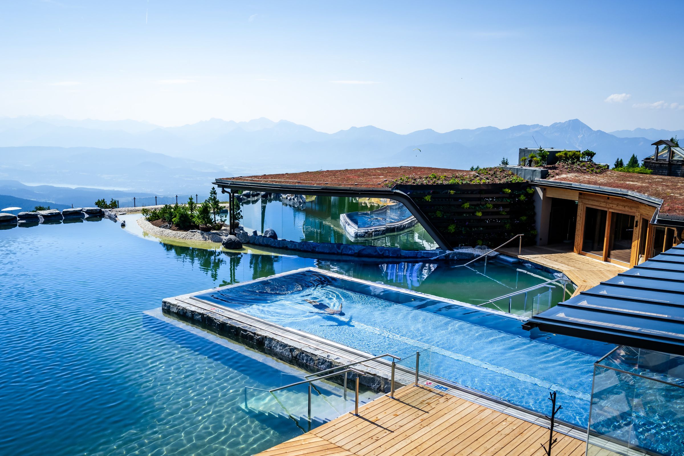 Infinity-Pool im Mountain Resort Feuerberg auf der Gerlitzen Alpe mit Naturbadeteich und Blick über Kärnten – Hotelfotografie
