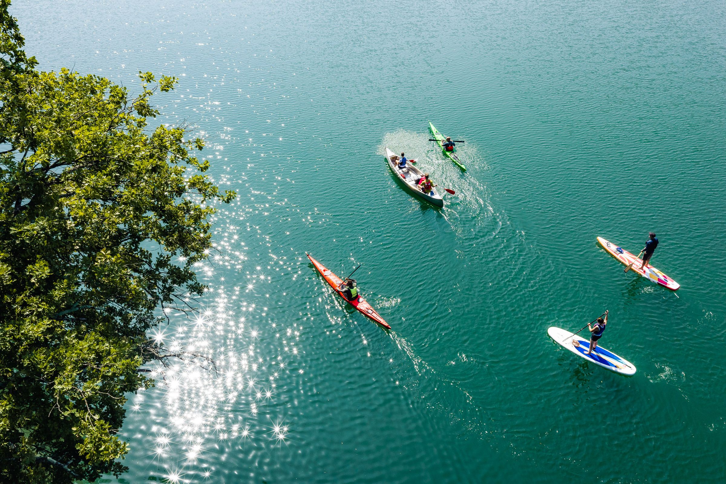 Kajaks, Kanu und Stand-up-Paddler am Draupaddelweg in Kärnten auf türkisblauem Wasser – Drohnenaufnahme für den Tourismus