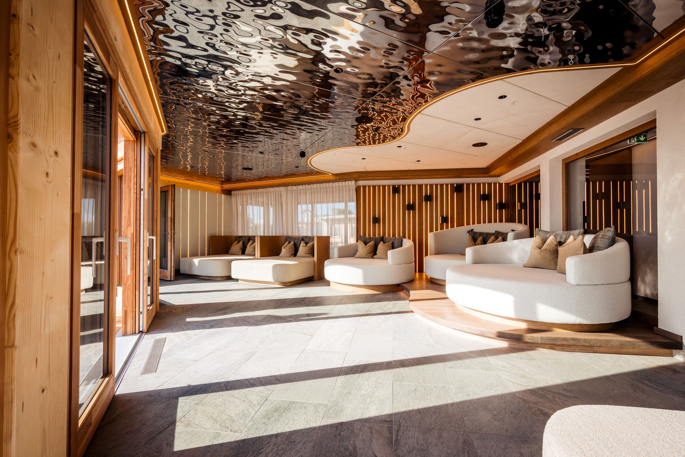 Ruheraum im Wellnessbereich des Mountain Resort Feuerberg mit Liegen, Holz und welliger Spiegeldecke – Architekturfotografie