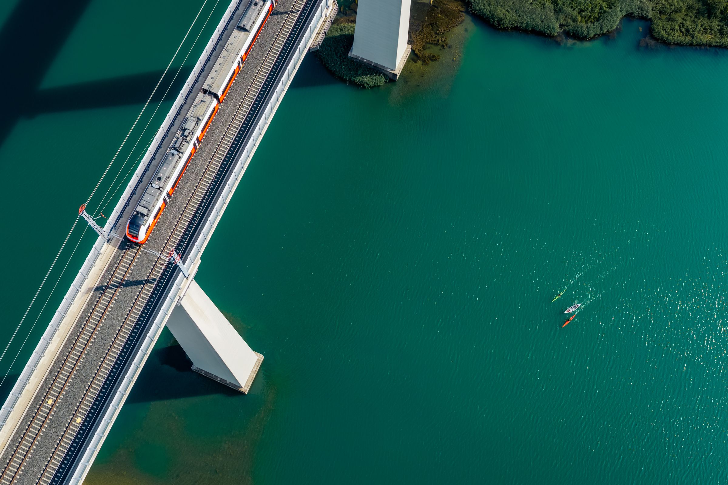 Zug der Koralmbahn auf der Brücke über die Drau, darunter Kajaks am Draupaddelweg – Drohnenaufnahme in Kärnten